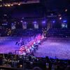 Riders on horseback carry the American flags in a parade as part of a show in an arena filled with an audience watching from tiered seating.