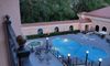 The image showcases a tranquil evening view of a pool area surrounded by patio furniture and lush greenery as seen from an overlooking balcony.