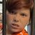 A child in an orange shirt with a dog print poses behind a fake jail cell in what appears to be a museum exhibit area.