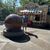 A man stands beside a large spherical fountain near an ice cream concession stand on a sunny day.