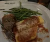 A plate of food featuring green beans, a meatball, and pasta with marinara sauce and grated cheese, accompanied by a glass of iced tea and some papers.