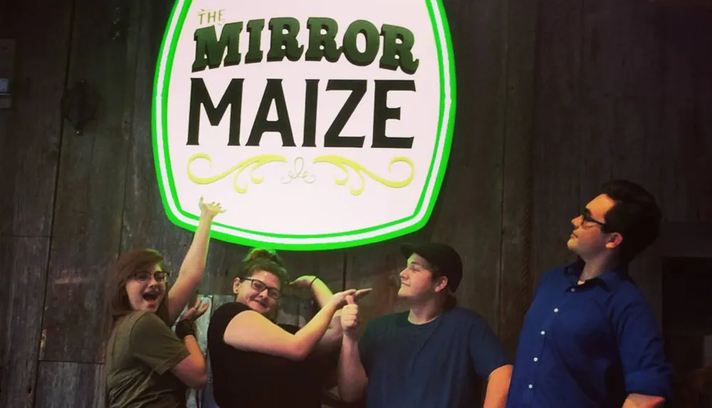 Four individuals pose playfully in front of a neon sign that reads The Mirror Maize