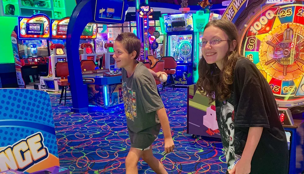 Two young people are smiling and enjoying themselves in a vibrant arcade filled with colorful game machines