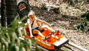 A child is enjoying a ride in an orange mountain coaster among the trees.