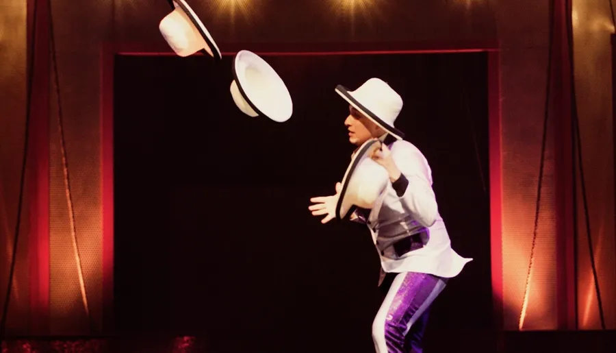 A performer in a white hat and costume is catching flying hats on stage, creating a dynamic and entertaining visual spectacle.