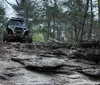 A red off-road vehicle is navigating a rocky creek bed with a person visible behind the roll bars engaged in an outdoor adventure