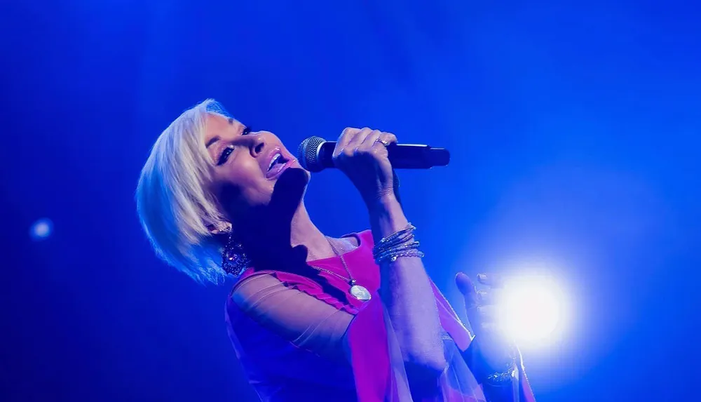 A singer passionately performs into a microphone under blue stage lighting