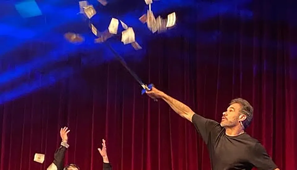 A performer is on stage throwing multiple cards into the air with a flourish using a wand