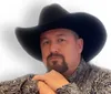 A smiling person in a cowboy hat holds a guitar up in the air against a soft-focus background