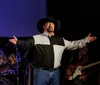 A smiling person in a cowboy hat holds a guitar up in the air against a soft-focus background