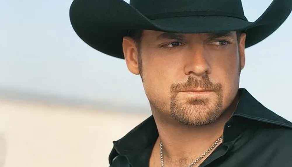 A man wearing a cowboy hat gazes intently at the camera against a blurred natural background