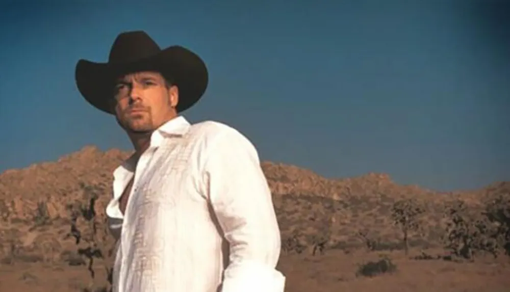 A man wearing a cowboy hat stands in a desert landscape