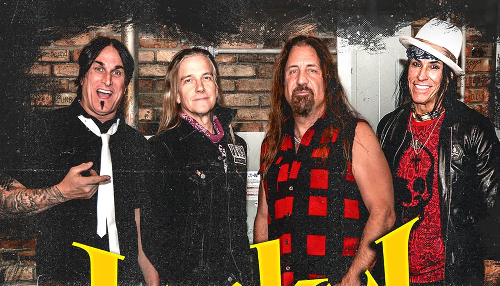 Four individuals likely members of a rock band stand together with lively expressions against a brick wall backdrop exuding a distinctly rock-and-roll vibe