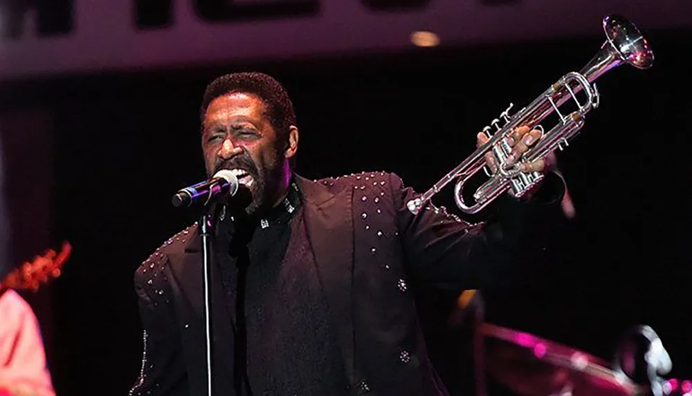 A musician sings into a microphone while holding a trumpet performing onstage