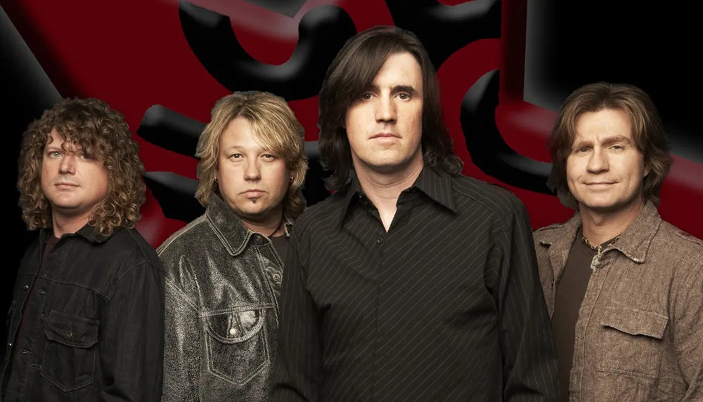 Four male band members are posing in front of a red and black abstract background