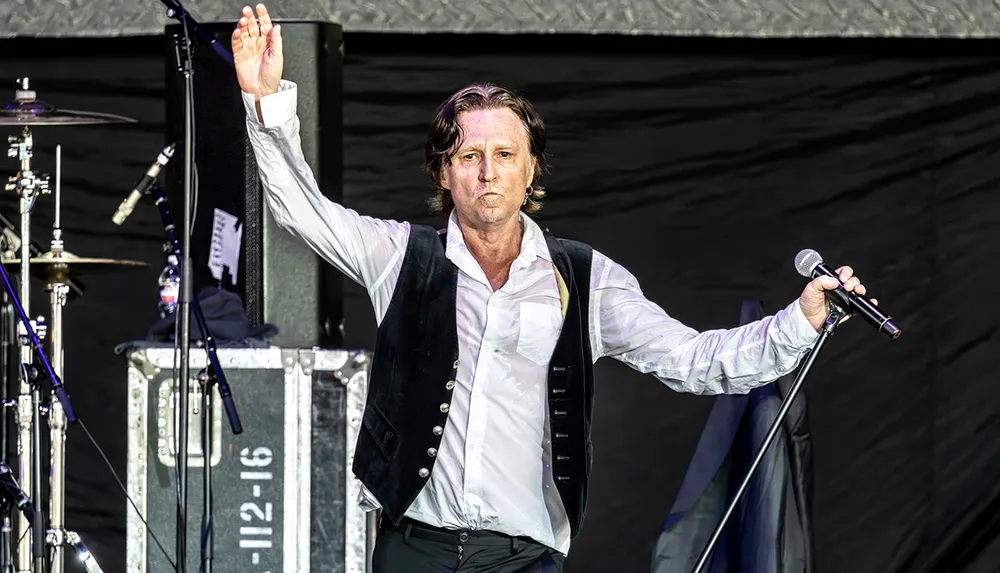 A man is performing on stage with a microphone in hand and one arm raised possibly signaling or engaging with an audience