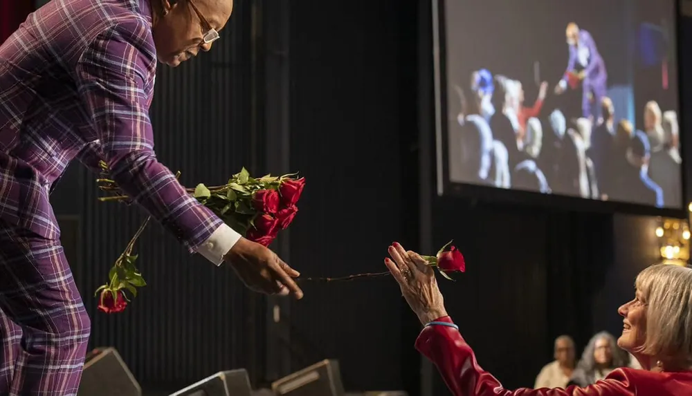 A person on stage is handing out roses to a member of the audience creating a moment of connection