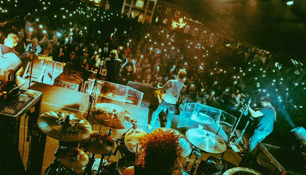 A band performs on stage in front of an audience illuminated by an array of smartphone lights