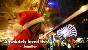 A child in a Santa hat looks longingly out of a window at night towards a brightly lit Ferris wheel, with the caption 