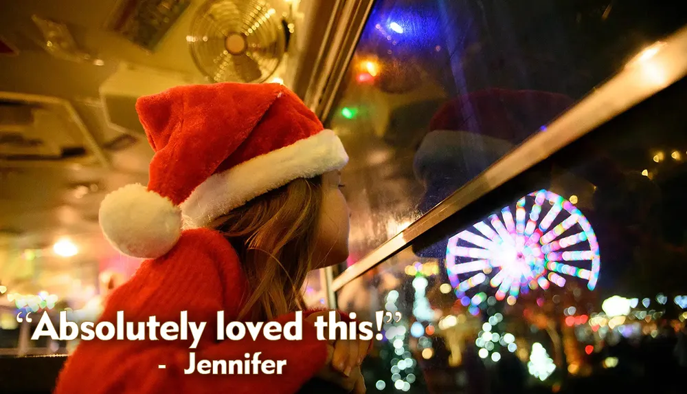 A child in a Santa hat looks longingly out of a window at night towards a brightly lit Ferris wheel with the caption Absolutely loved this - Jennifer