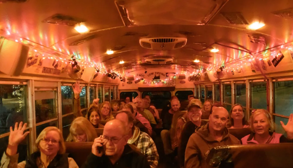 A group of cheerful people is riding in a festively decorated bus with string lights and signs appearing to enjoy a group outing or event