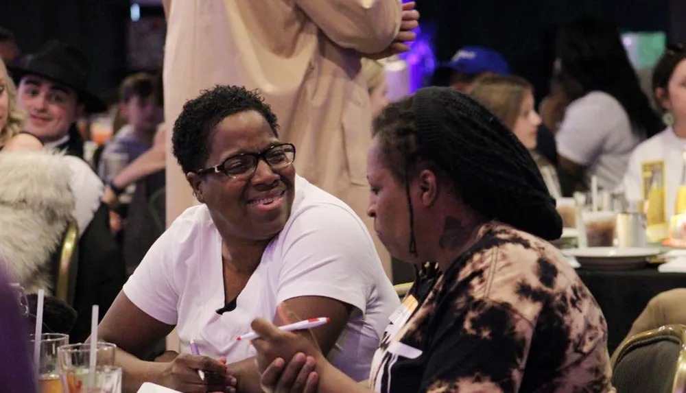 Two individuals are engaged in a cheerful conversation at an indoor event