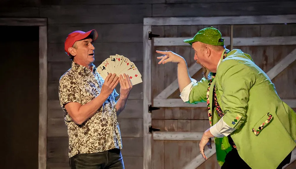 Two performers are engaged in a comedic magic routine one holding a fan of playing cards while the other gestures dramatically