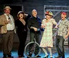 A group of eight people in colorful attire is joyfully posing on a stage with one person holding a guitar and another with a unicycle