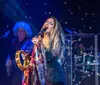 A singer passionately performs on stage holding a tambourine with band members playing instruments in the background