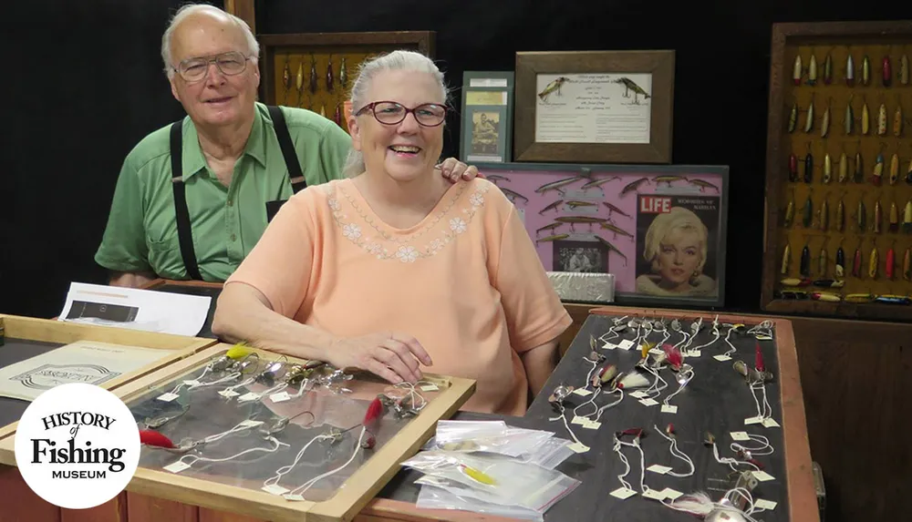 A smiling couple stands behind display cases filled with fishing lures at the History of Fishing Museum