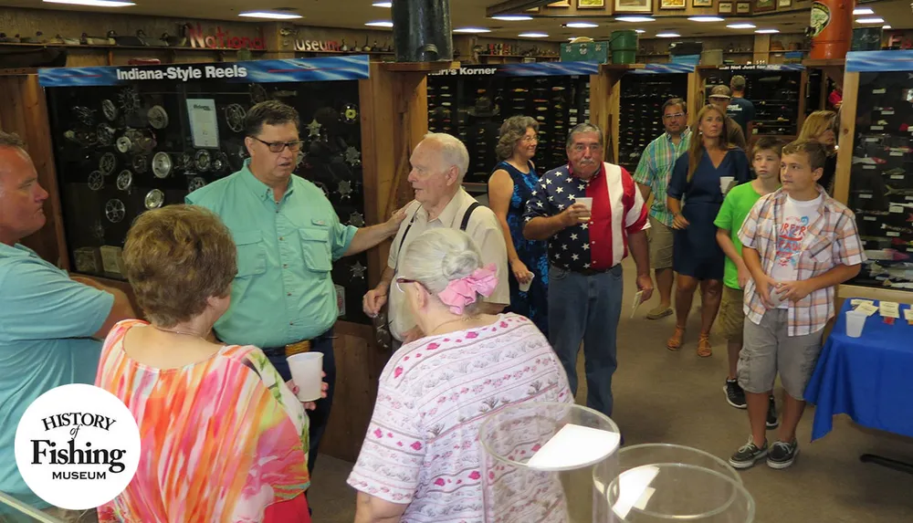 A group of people are gathered in a fishing history museum socializing and observing Indiana-style reels on display