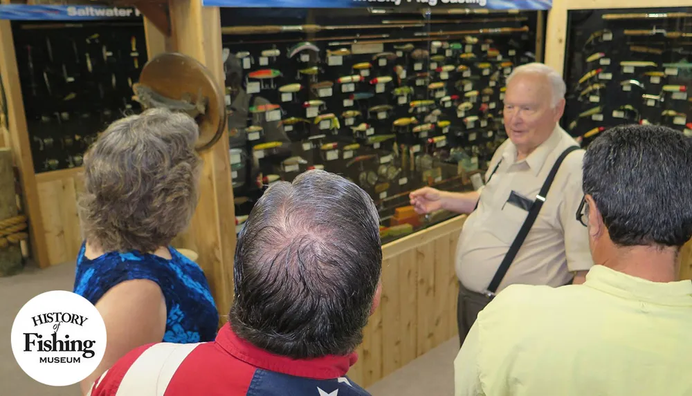 A group of people is engaged in a discussion at the History of Fishing Museum observing a display of fishing lures