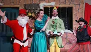 Four people are dressed in colorful and theatrical Christmas-themed costumes, expressing exaggerated emotions in what appears to be a festive play or performance.