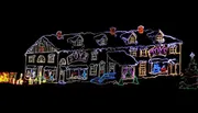 This image shows a house elaborately decorated with colorful Christmas lights, featuring outlines of the architecture and festive motifs such as the word 