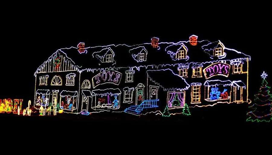 This image shows a house elaborately decorated with colorful Christmas lights, featuring outlines of the architecture and festive motifs such as the word TOYS, a toy soldier, and a Christmas tree.