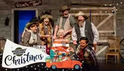 A group of people in Western wear are joyfully posing on a rustic set, embodying the festive spirit of a Christmas-themed event or production.