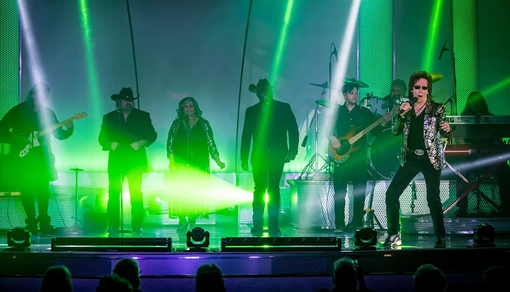 A band performs on stage amid vibrant green lighting and haze effects with a dynamic lead singer taking center stage